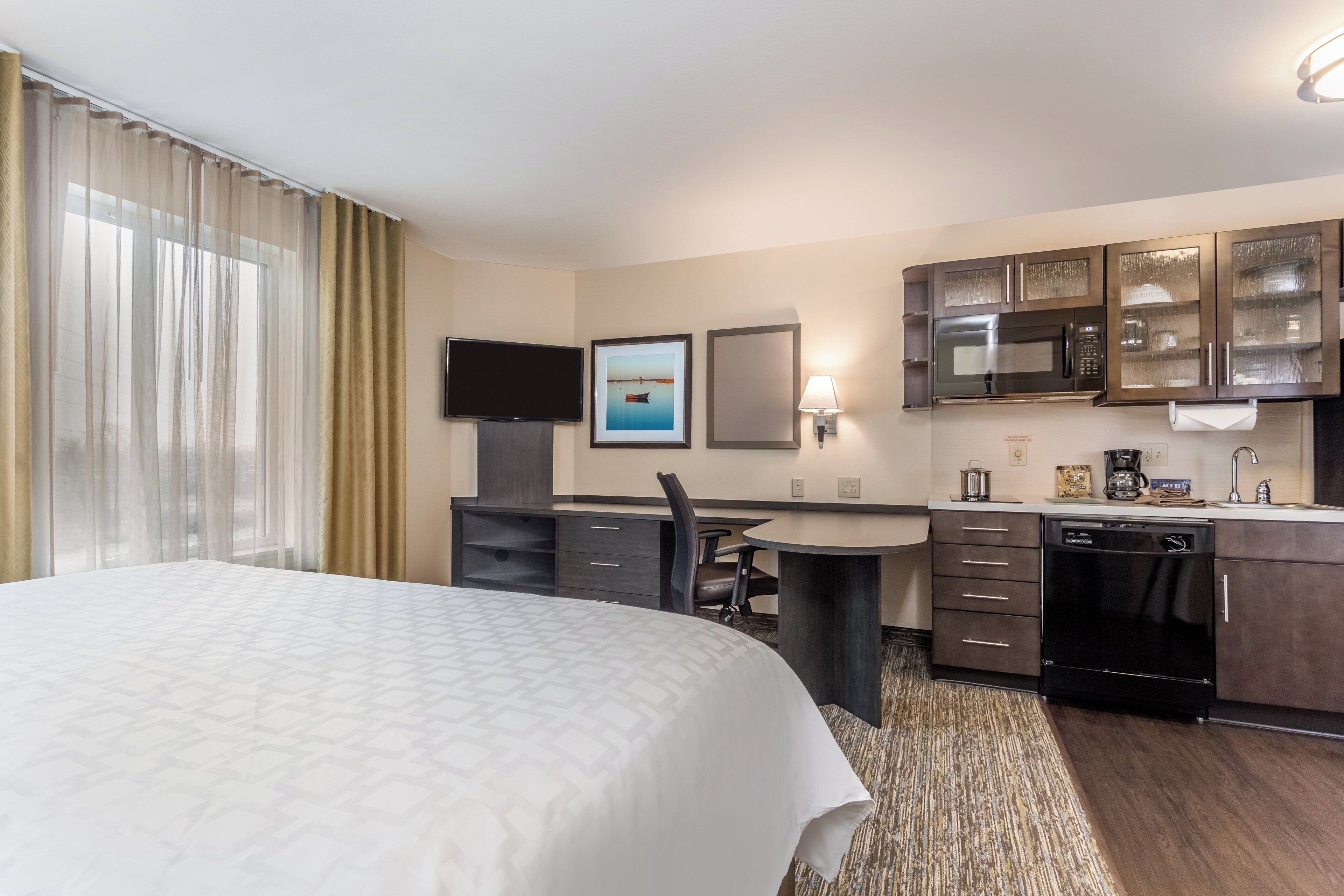 A hotel room with a bed, a desk, a chair, a television, a microwave, and a coffee maker.