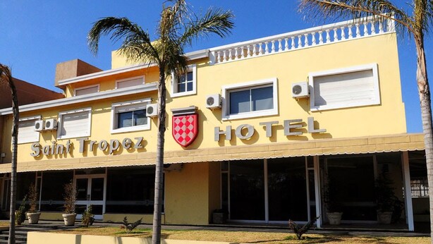 A hotel named Saint Tropez with a yellow facade, large windows, and a red and white checkered logo. - Hotel Saint Tropez (Villa Carlos Paz)