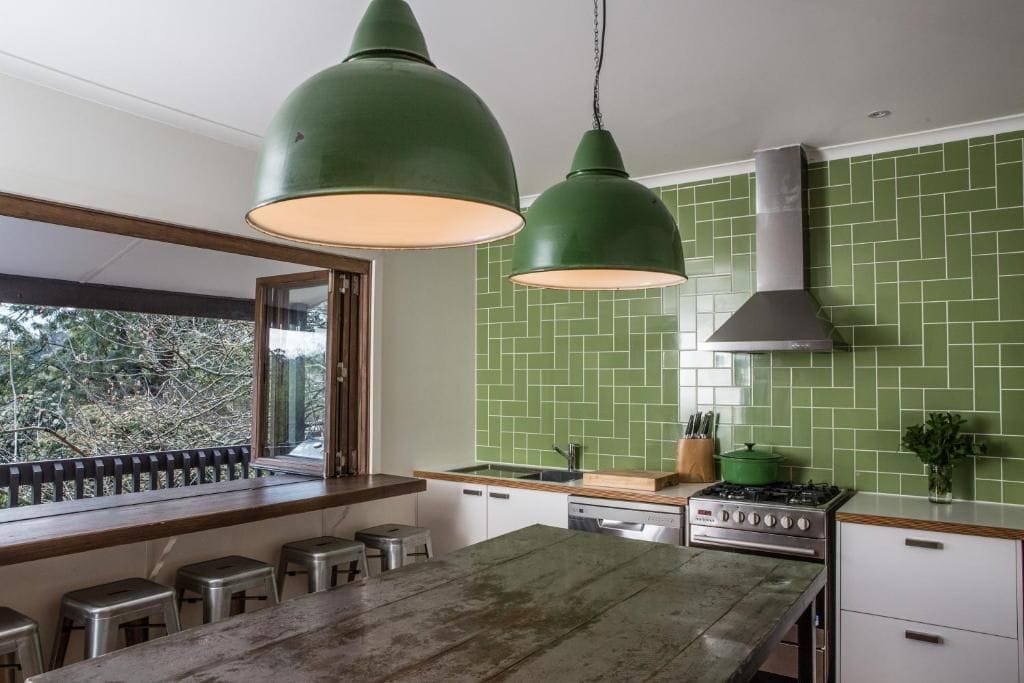 Cozinha com ilha grande, luminárias pendentes verdes e vista pela janela.