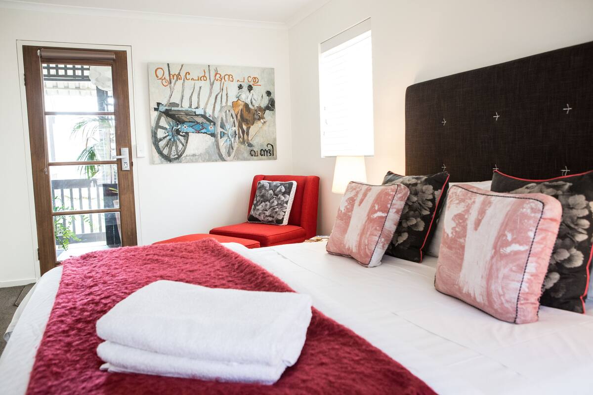 A bedroom with a large bed, a red chair, and a painting on the wall.