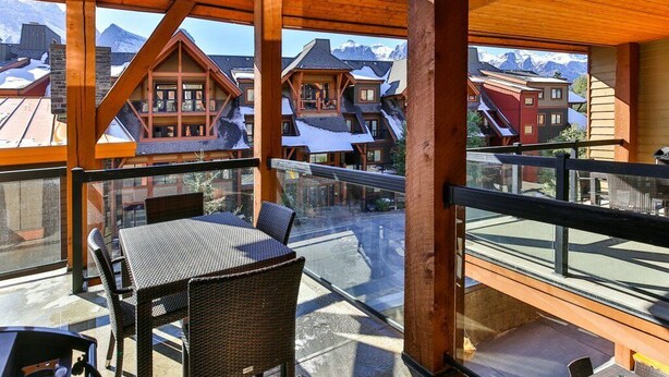 A balcony with wicker furniture overlooking a mountain village. - Bow 221 | Resort Suite with Pool & Hot Tub (Canmore)