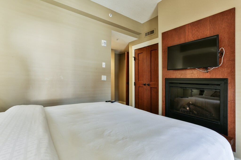 A hotel room with a large bed, a television mounted on the wall, and a fireplace.