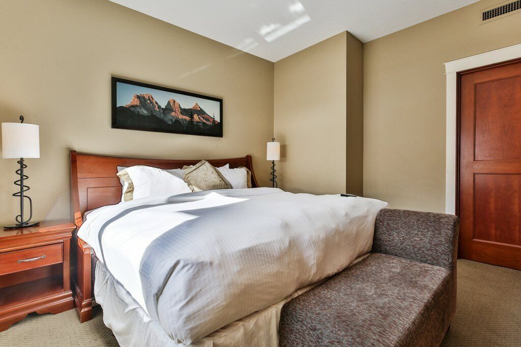 A hotel room with a large bed, two bedside tables with lamps, a framed picture on the wall, and a wooden door.