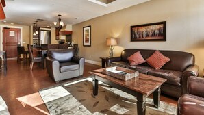 A spacious living area with a leather sofa, a coffee table, and a dining area in the background. - Bow 221 | Resort Suite with Pool & Hot Tub (Canmore)