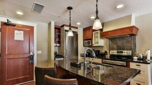 A kitchen with a central island, stainless steel appliances, and a hanging light fixture. - Bow 221 | Resort Suite with Pool & Hot Tub (Canmore)
