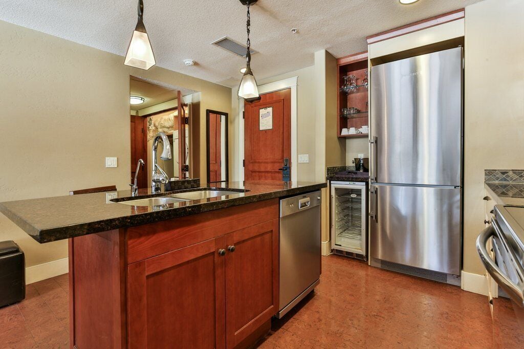 A kitchen with wooden cabinets, a stainless steel refrigerator, a dishwasher, and pendant lighting.
