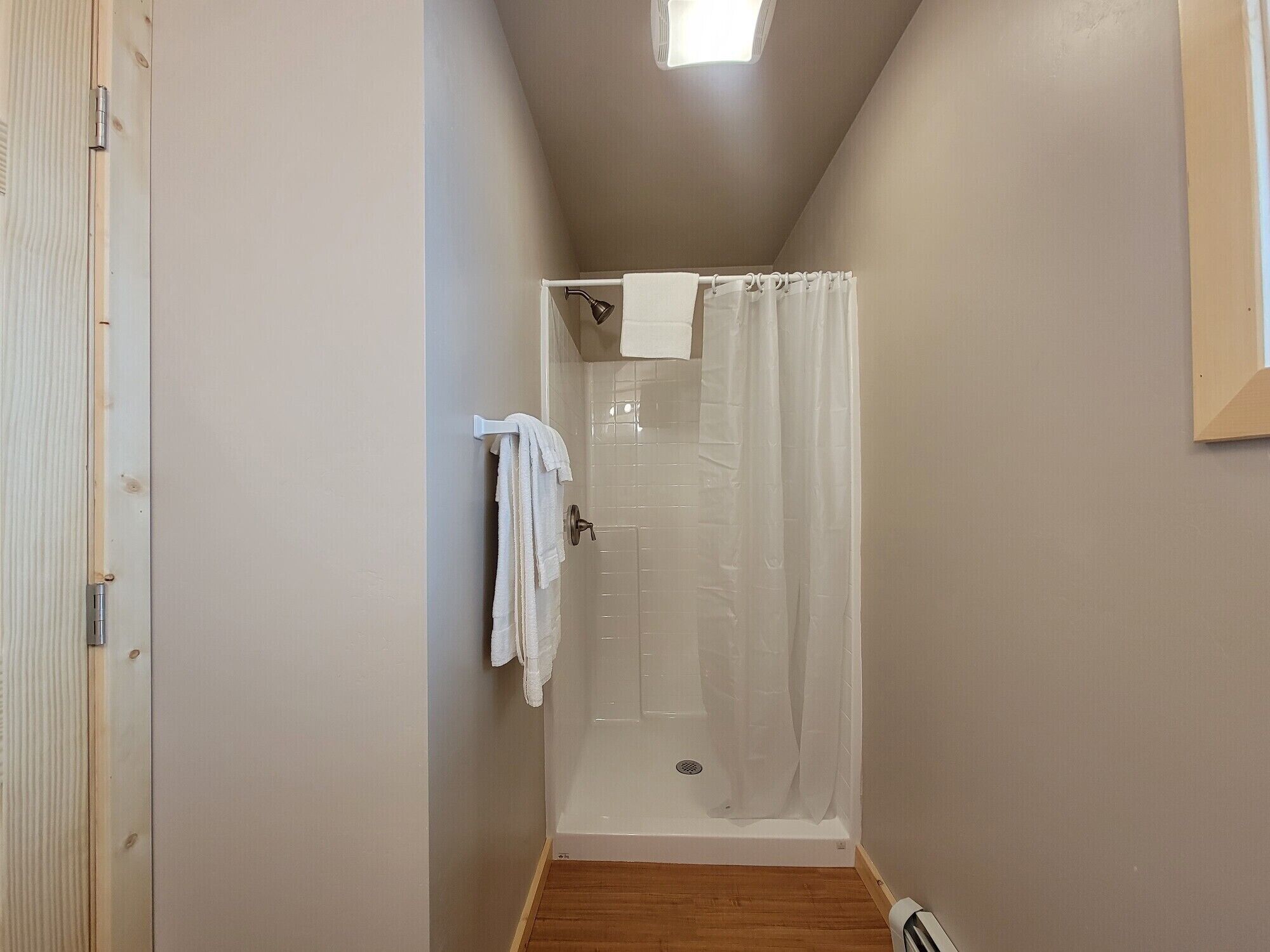 Un baño pequeño y estrecho con ducha y suelo de madera.