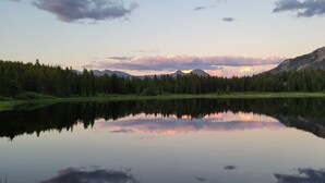 Un lago tranquilo que refleja árboles y montañas, rodeado de un área boscosa.