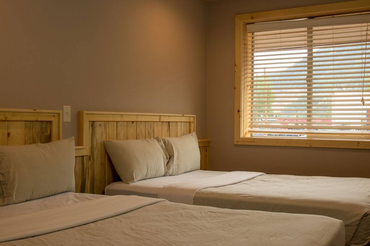 A bedroom with two beds, wooden headboards, and a window with blinds.