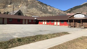 Un motel con fachada roja y blanca, un estacionamiento y montañas al fondo.