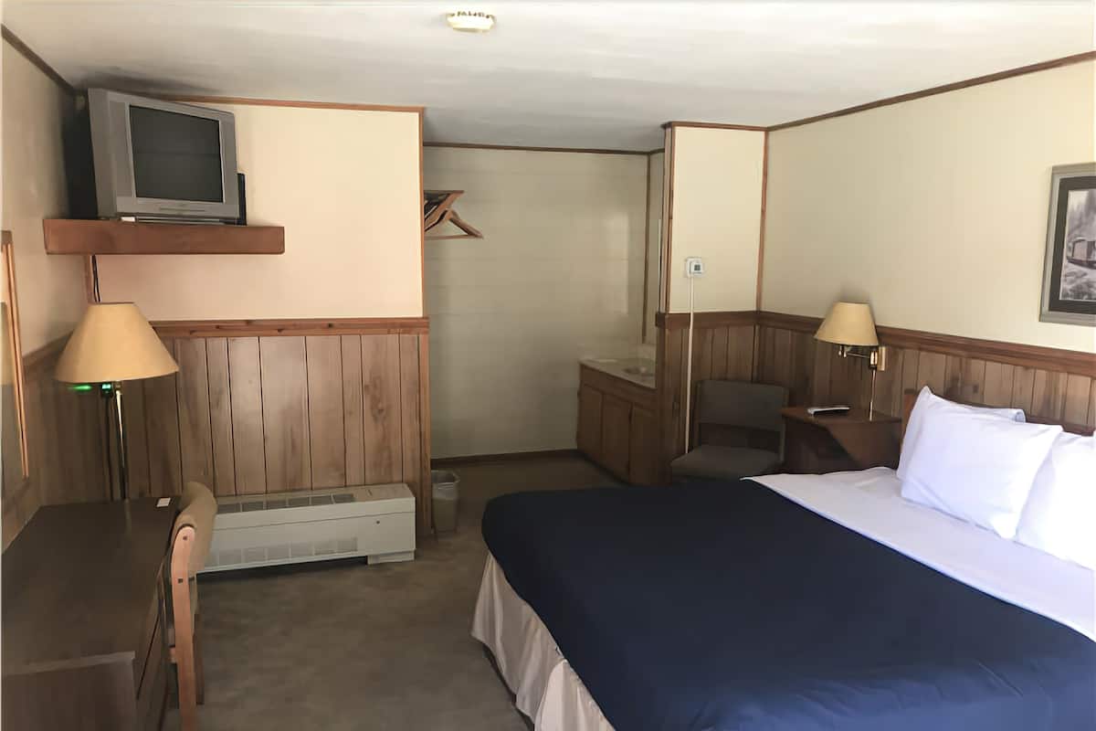 A hotel room with a bed, a desk, a chair, a television, and a lamp.