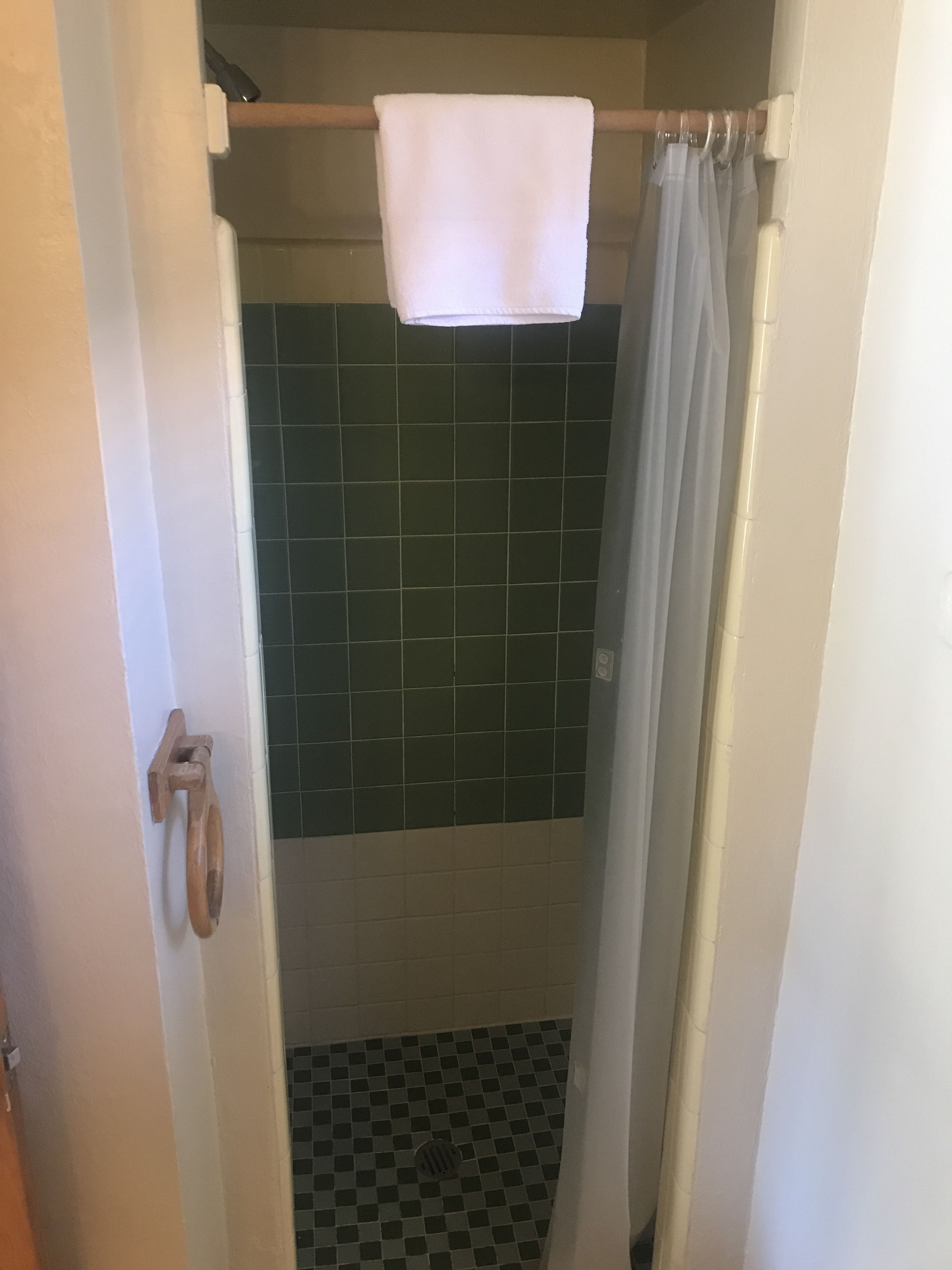 Un baño con ducha, una toalla colgada en un perchero y un picaporte.