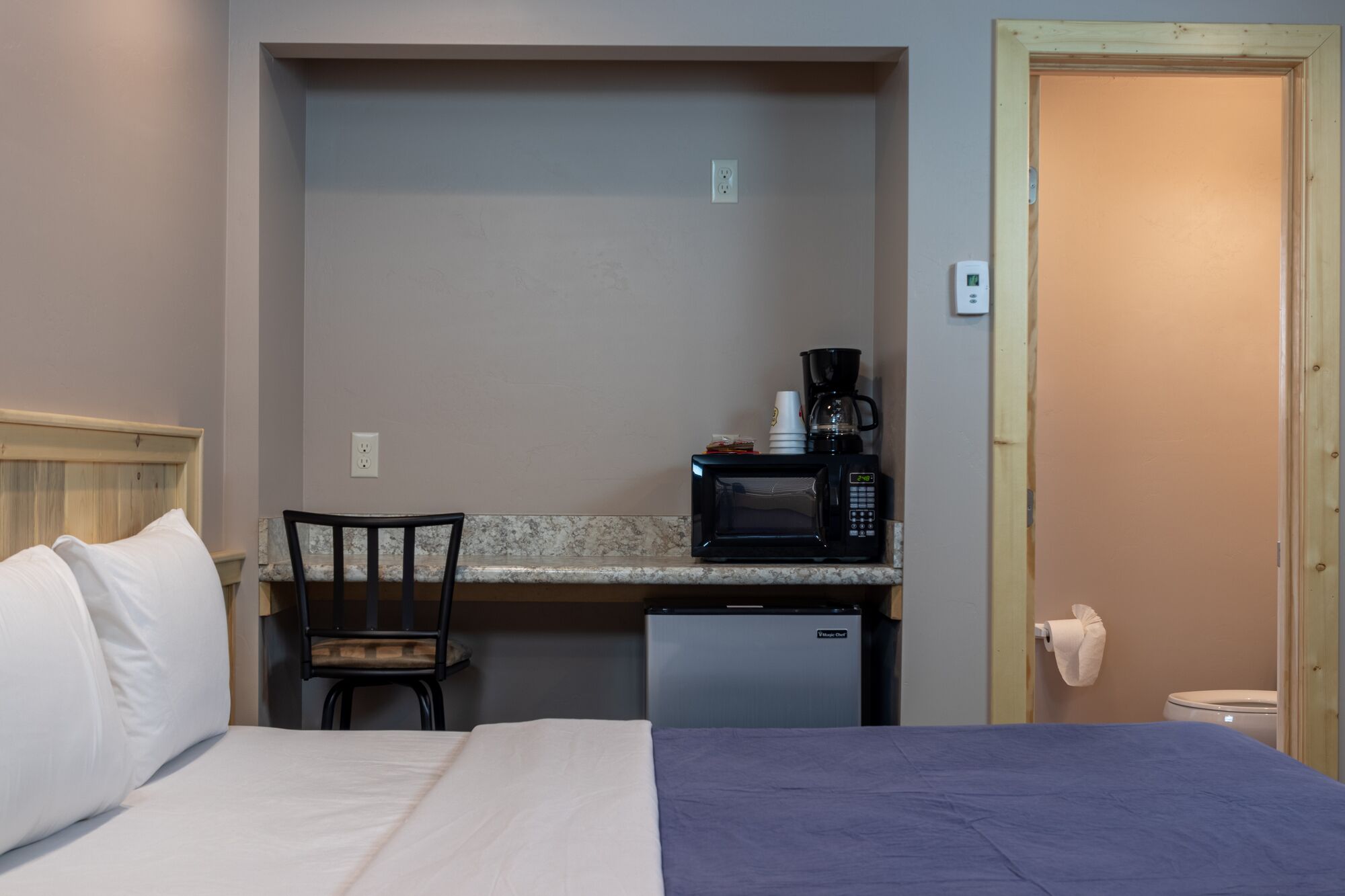 Habitació d'hotel senzilla amb un llit, una cuineta petita que inclou un microones, una cafetera i un mini-frigorífic.