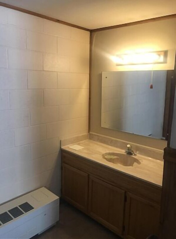 A small bathroom with a white tiled wall, a wooden vanity, a mirror, and a built-in air vent.