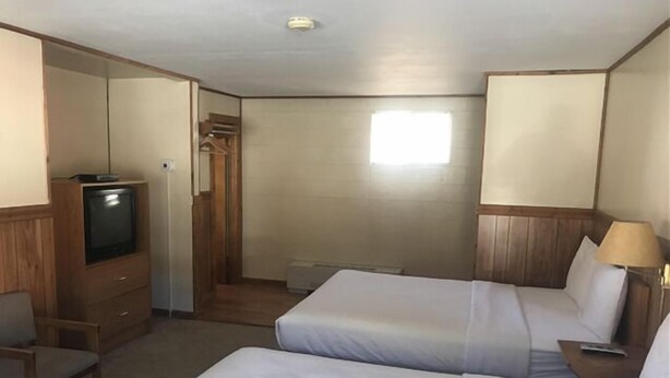 Habitación de hotel con dos camas, televisión, una silla y escritorio.