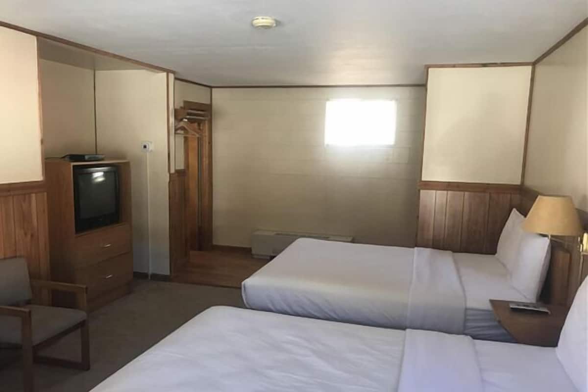 A hotel room with two beds, a TV, a chair, and a desk.