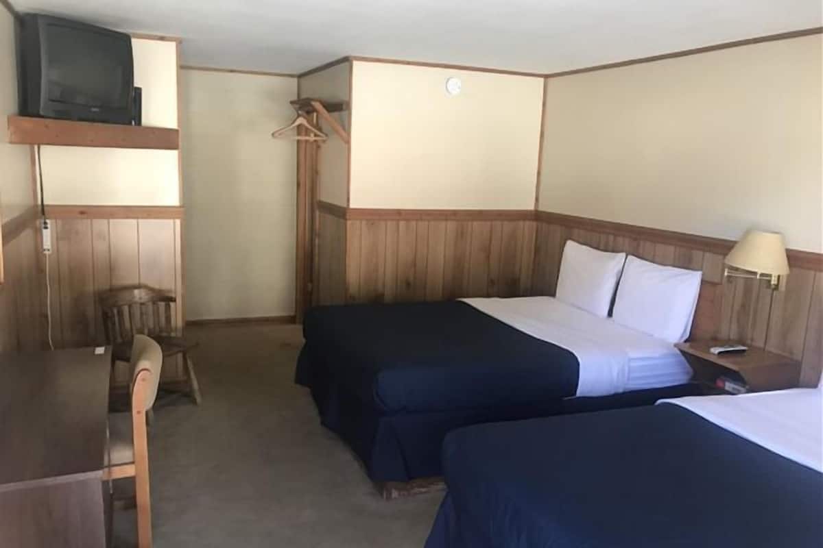 A hotel room with two beds, a desk, a chair, a TV, and a lamp.