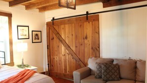 A bedroom with a bed, a nightstand, a lamp, a wooden barn door, and a beige sofa with patterned cushions. - The Rustic Old Farmhouse Peaceful home in Amish country,10 min from tourist area (Gap)