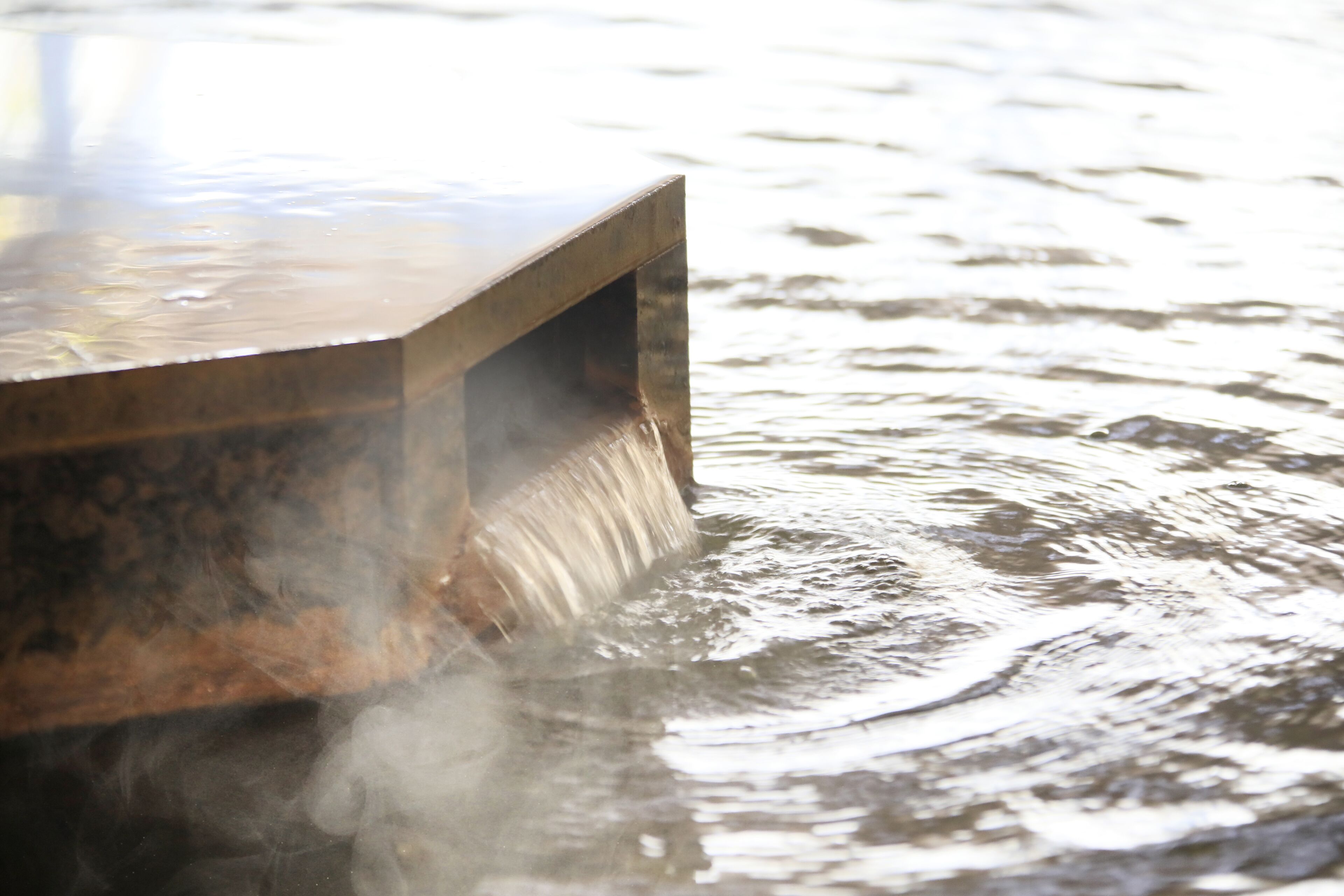 A metal structure partially submerged in water with steam rising from it.