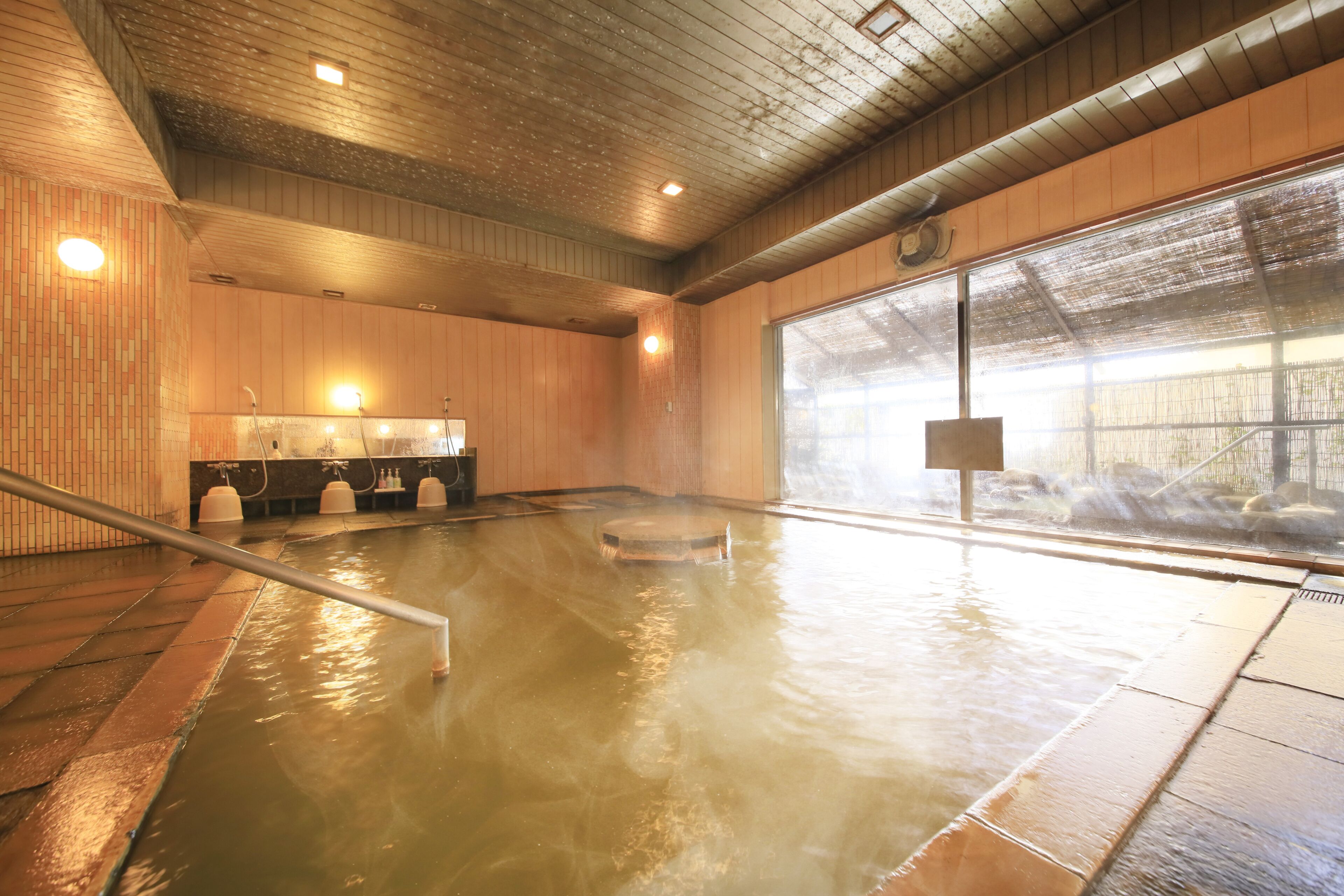 Un baño de aguas termales con paredes de madera, piso de baldosas, techo de madera y un ventanal grande.