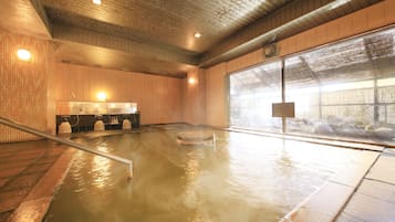 Un baño de aguas termales con paredes de madera, piso de baldosas, techo de madera y un ventanal grande.