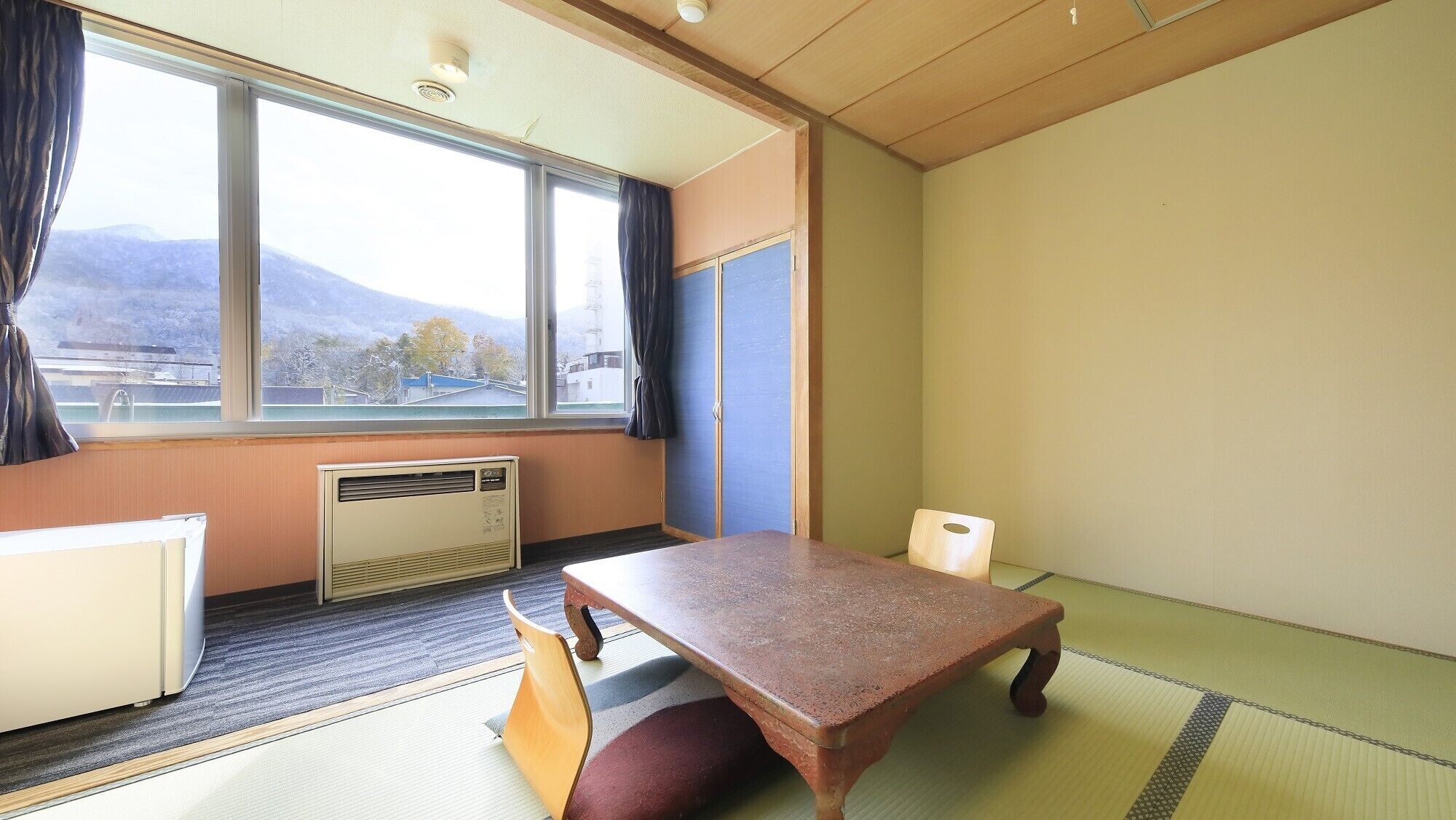 Une pièce avec un sol recouvert de tatamis, une table en bois, un radiateur et une fenêtre donnant sur les montagnes.