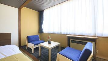 Ein Hotelzimmer mit einem Bett, einem Schreibtisch, einem Sessel und einer Couch. Ein Fenster mit Vorhängen und ein kleiner Tisch mit einer Vase.