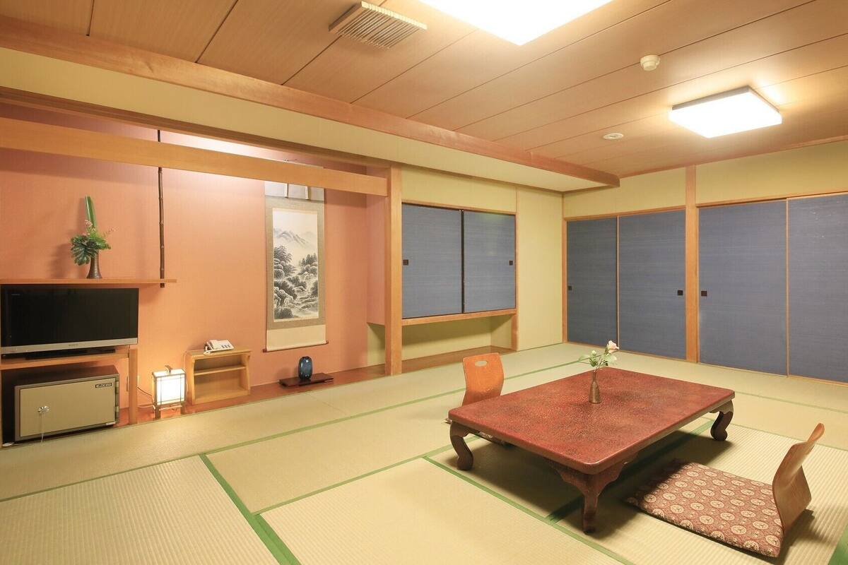A traditional Japanese room with tatami flooring, a tatami mat table, a television, a cabinet, and sliding doors.