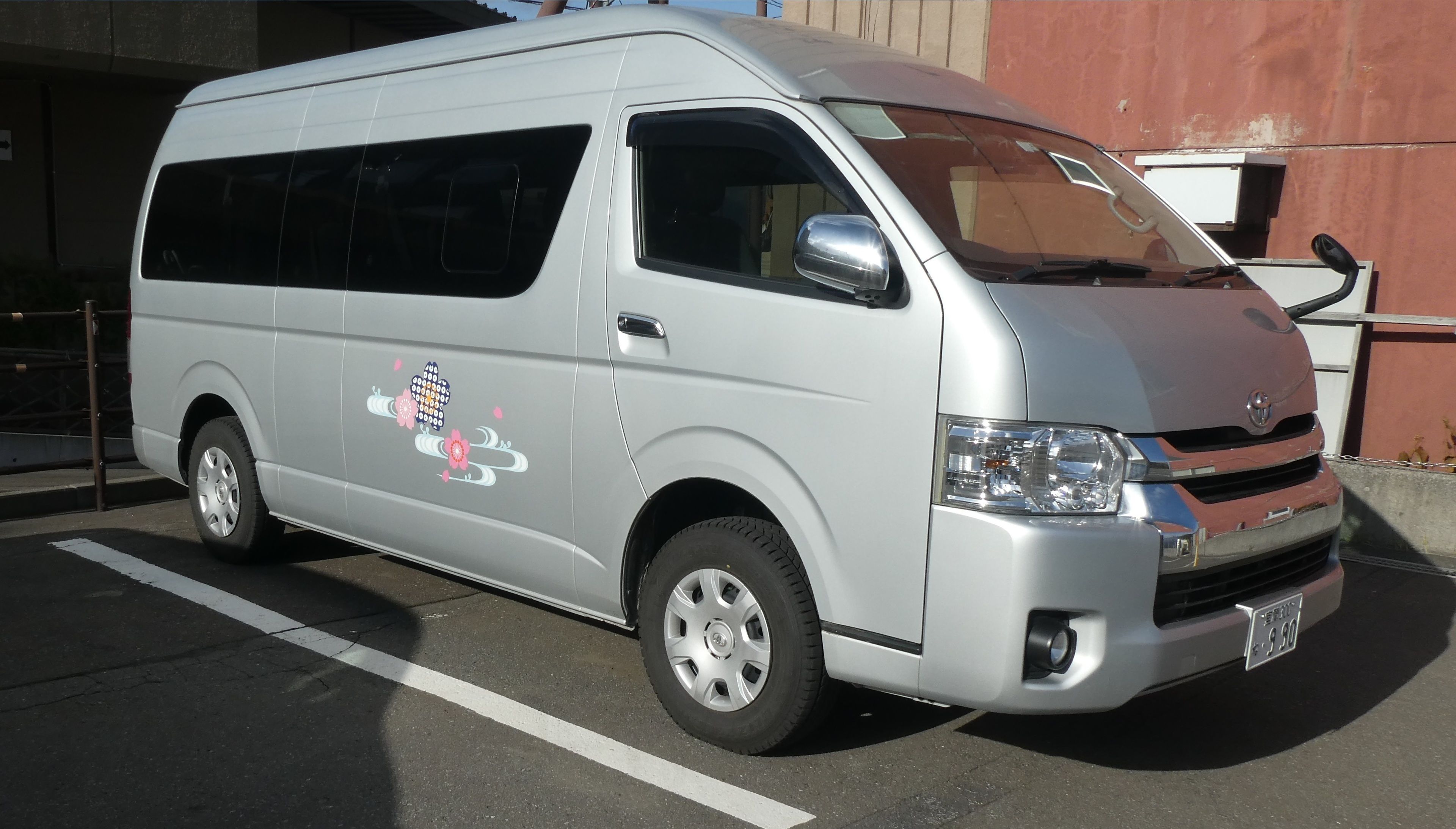 Un fourgon argenté était stationné sur un parking, orné d’un motif floral décoratif sur le côté.