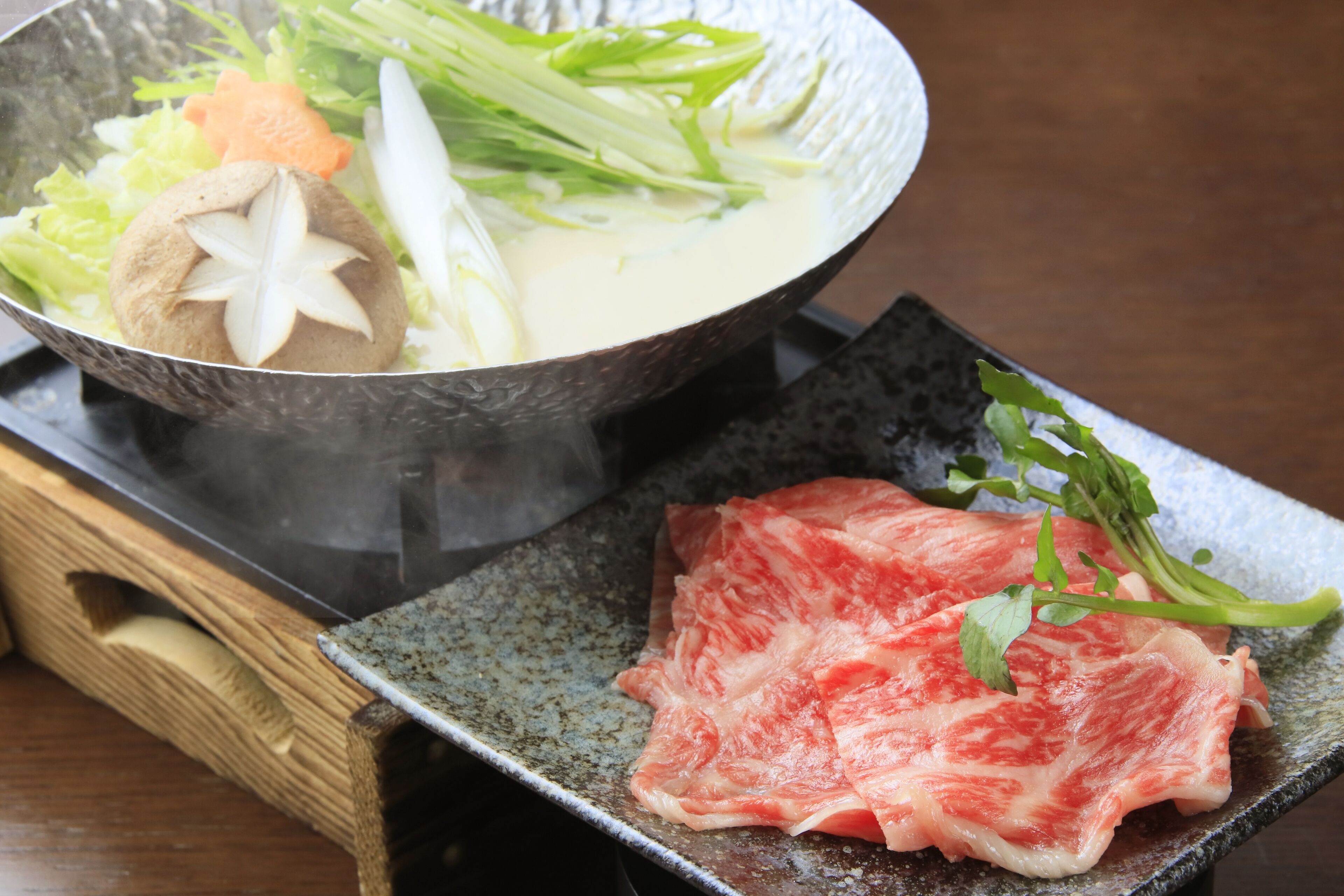 A bowl of soup with vegetables and a piece of meat on a plate.