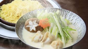 A bowl of soup with vegetables and meat, and a plate of noodles in the background.