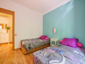 A bedroom with two beds, a bedside table with a lamp, a dresser, and a window with a plant. - ABSOLUTE SAGRADA FAMILIA // Standard // (Barcelona)