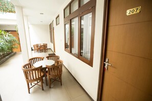 A corridor with a wooden door labeled 207, a dining area with wooden chairs and a table, and a window with curtains.