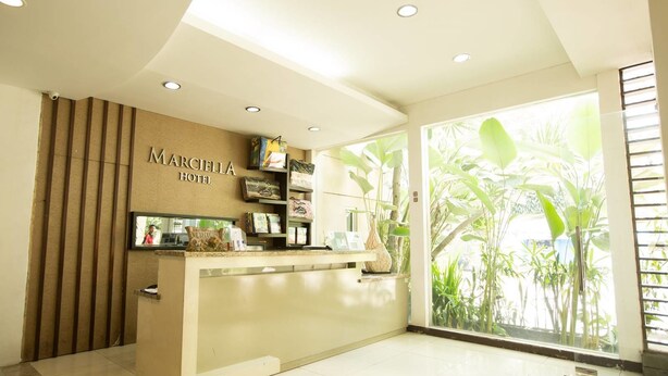 A hotel reception area with a modern design, a reception desk, and a large window offering a view of lush greenery.