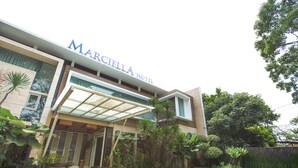 The Marcella Hotel with a modern design, featuring a glass entrance canopy and lush greenery around the building.