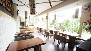 A restaurant with wooden tables and chairs, large windows, and hanging decorative lamps.