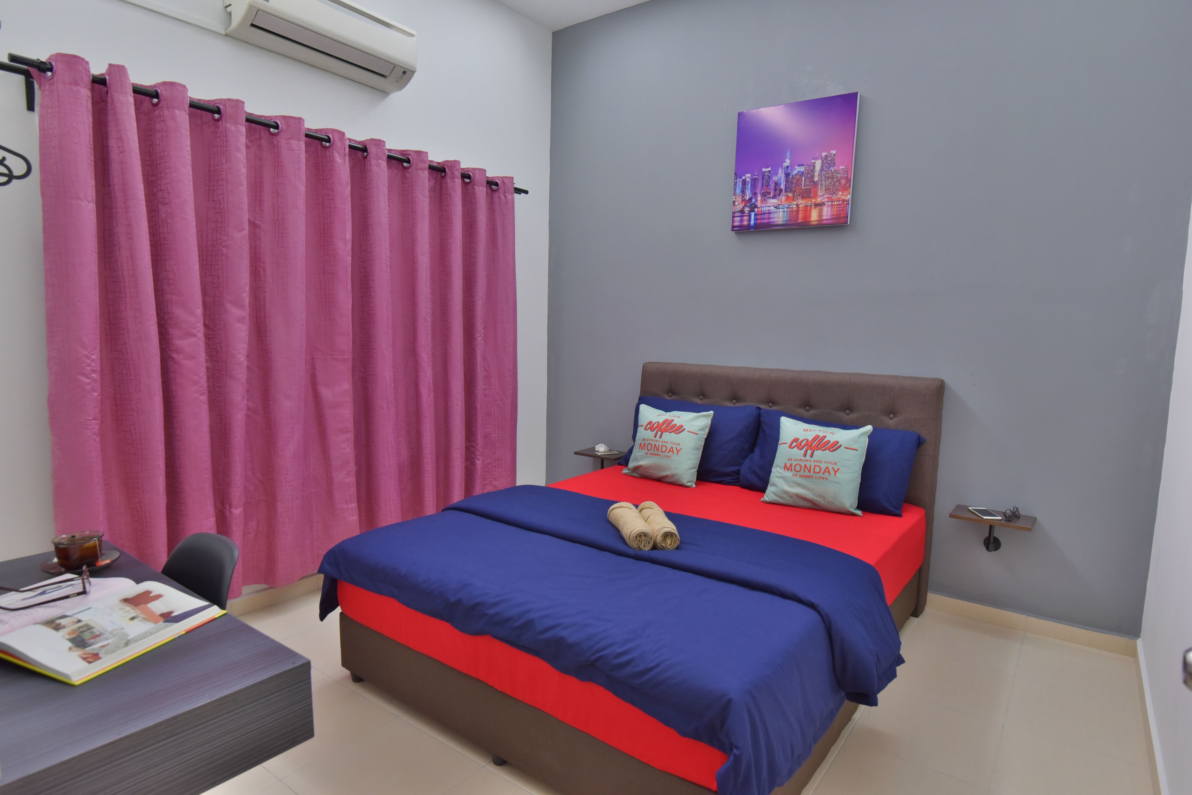 A bedroom with a bed, a desk, a chair, a window with pink curtains, and a cityscape painting on the wall.
