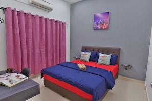 A bedroom with a bed, a desk, a chair, a window with pink curtains, and a cityscape painting on the wall.
