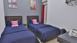 Camera d'albergo con due letti, una scrivania e una sedia. Si notano due quadri appesi al muro, una tenda rossa e un condizionatore d'aria.