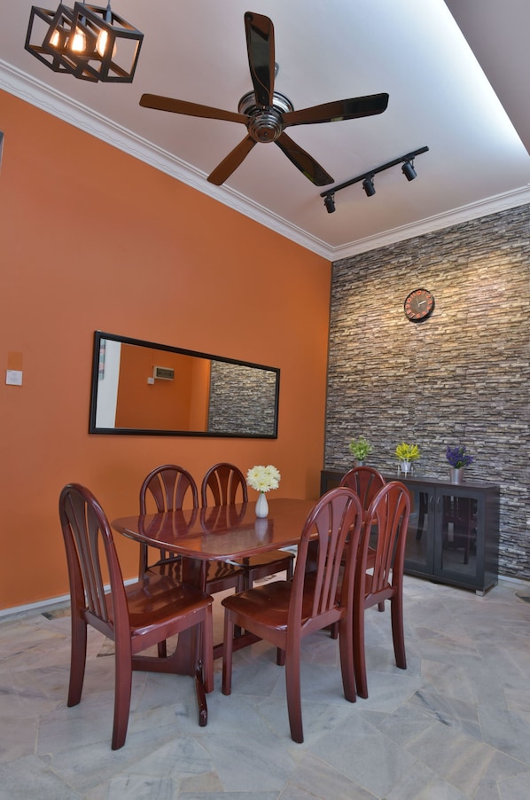 A dining area with a round table, six chairs, a ceiling fan, and a stone wall with a clock.