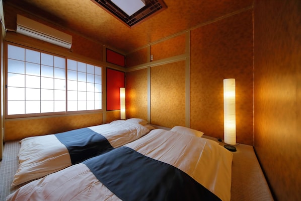A hotel room with two beds, a large window with a view, a wall-mounted air conditioner, and a bedside lamp.