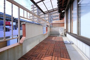 A covered balcony with a brick floor, metal railings, and a view of a building with a tiled roof.