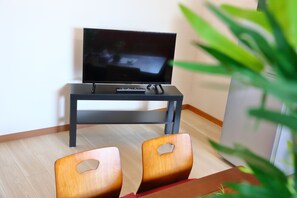 A living room with a flat-screen TV on a stand, two wooden chairs, and a plant.
