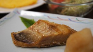 A close-up of a cooked meat dish on a plate, with a salad and another dish in the background. - Yakehashiri Cabin Village (Hachimantai)