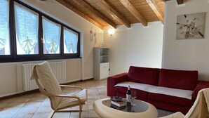 Un salon avec un canapé rouge, un fauteuil blanc, une table basse ronde et un plafond en bois.