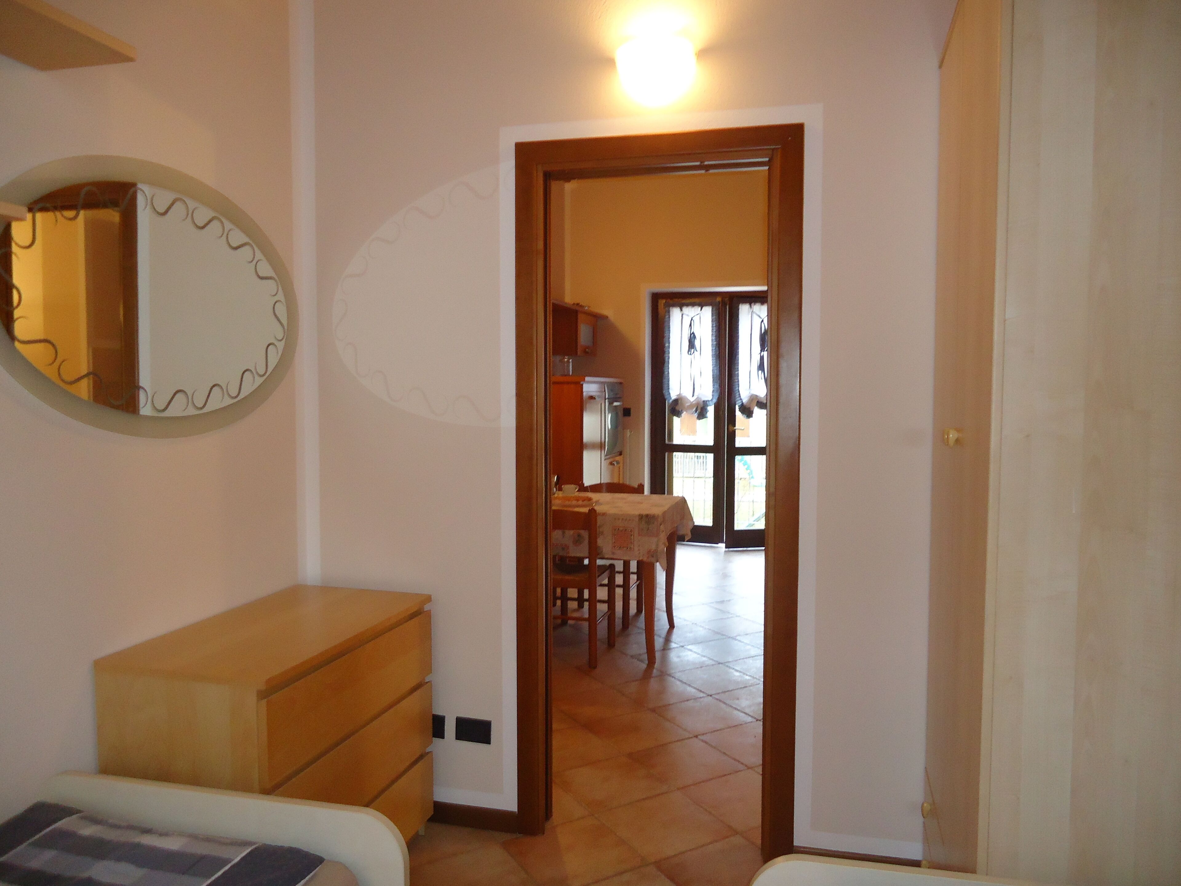 Une pièce comprenant une commode en bois, un miroir et une porte donnant sur un coin repas avec une table et des chaises.