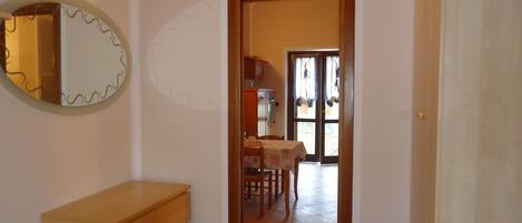 Une pièce comprenant une commode en bois, un miroir et une porte donnant sur un coin repas avec une table et des chaises.