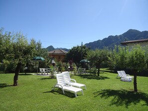 A grassy outdoor area with white lounge chairs, a small table, and umbrellas. - Casa Vittoria type V1, up to 5 people, garden, only 200m to the lake / beach (Crone)