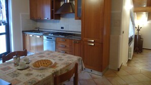 Une cuisine avec des meubles de rangement en bois, une cuisinière et une table à manger sur laquelle se trouve une tarte.