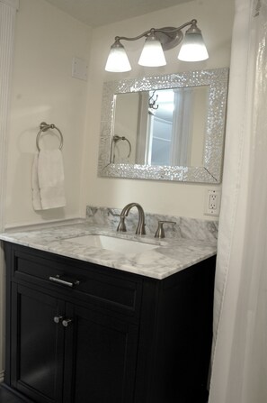 A bathroom with a marble sink, black cabinets, a towel ring, and a mirror with a decorative frame. - New! Victorian Apartment. Park & Walk Everywhere in Town (St. Augustine)